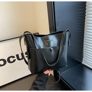 Detail of black faux leather bucket bag with magnetic front pocket and gold logo lettering