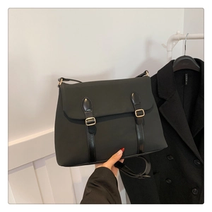 Detail of black tote bag featuring glossy straps with golden metal buckles and flap design