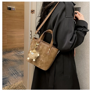Detailed view of brown quilted bucket bag with a fuzzy doll charm on a leather strap