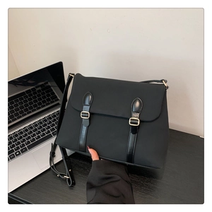 Close-up of black frosted messenger bag with gold buckles on a desk with a laptop