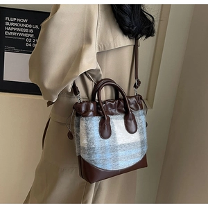 Sac seau en cuir marron et laine à carreaux porté en bandoulière sur un trench beige