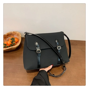 Detail of black satchel bag with parallel decorative straps and golden buckles