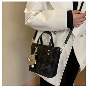 Detail of black quilted bucket bag featuring golden hardware and brown plush charm accessory