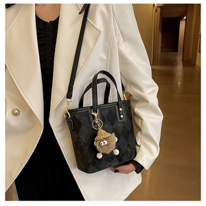 Detail of black checkered leather bucket bag with a cute brown plush monster charm