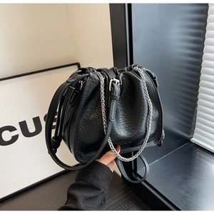 Detail of black drawstring bucket bag with pleated texture and silver chain strap