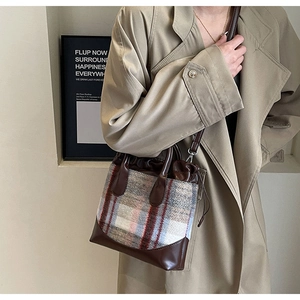Détail d'un sac seau vintage en laine à carreaux porté avec un trench-coat kaki