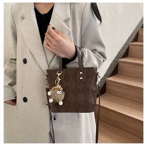 Detail of dark brown quilted leather tote bag with plush charm on a long coat model