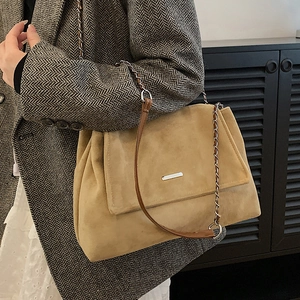 Beige suede tote bag with chain strap and metal detail shown on an elegant model