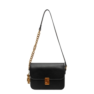 Classic black leather crossbody flap bag with gold hardware and bear charm on white background