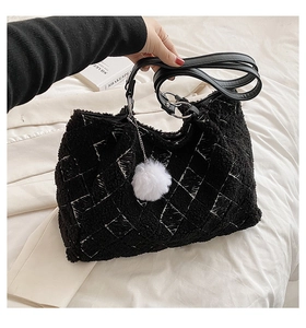 Detail of black faux shearling tote bag featuring white plaid patterns and furry pompom