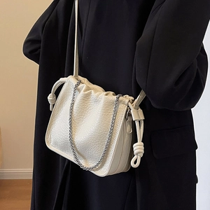Chic beige pleated bucket bag with silver chain strap shown on a black winter coat