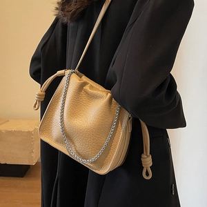 Chic khaki bucket bag with pleated texture and silver chain strap shown on a black coat