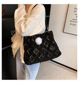 Detail view of black faux shearling tote bag featuring white quilted pattern and pompom charm