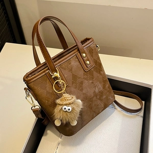 Brown quilted bucket bag with plush charm on a white gift box, 45-degree view
