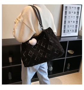 Detail of plush black tote bag with white quilted pattern and fluffy pompom charm