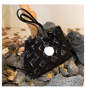 Detail of black faux fur tote bag with white grid pattern and plush ball charm in a nature scene