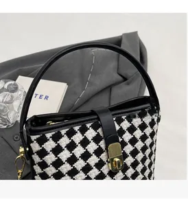 Détail du sac seau en pied-de-poule avec bordure en cuir noir et fermoir métallique doré