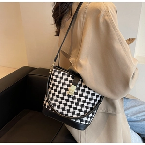 Détail du sac seau à damier avec boucle dorée porté sur un trench-coat chic
