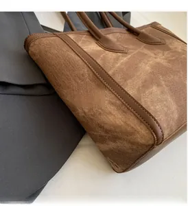Detail of a brown tote bag with leather straps and washed canvas texture on a gray suit