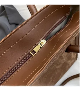 Close-up of golden smooth zipper and brown lychee grain leather stitching on tote bag