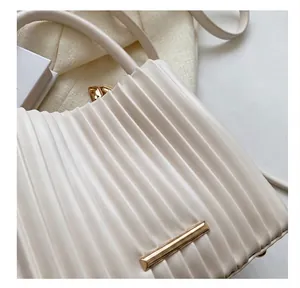 Gros plan sur la texture plissée verticale et les détails dorés du sac seau beige