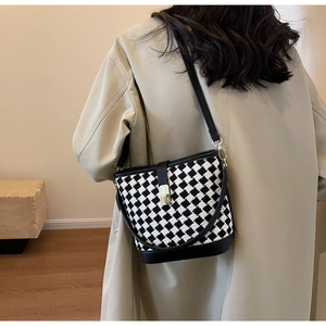 Détail d'un sac seau en tweed avec garniture en cuir et fermoir doré porté par un mannequin