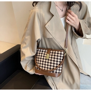 Détail d'un sac seau à carreaux marron porté à l'épaule avec un trench-coat classique