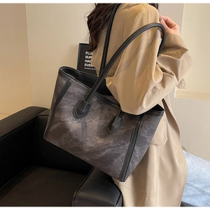 Detail of stone-patterned grey tote bag with black leather straps on shoulder