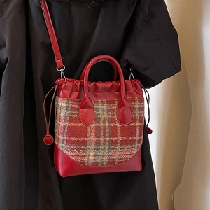Sac seau en tweed à carreaux rouges avec poignées rondes porté sur un manteau noir