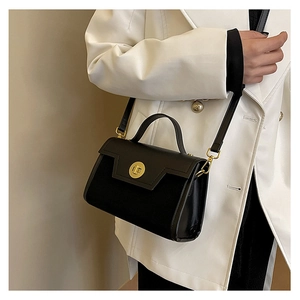 Detail of black structured shoulder bag with geometric flap and gold metal twist lock