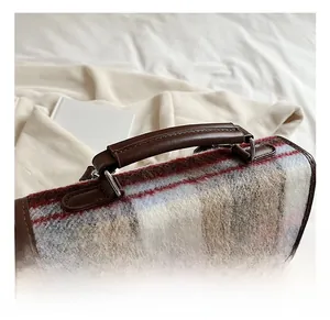 Detail of checkered tweed bag featuring brown leather handle and vintage metal hardware
