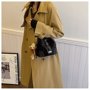 Détail du sac seau noir matelassé avec breloque ours en peluche sur un trench-coat