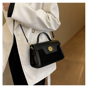Detail of black crossbody bag with gold round lock and matte leather texture on a model