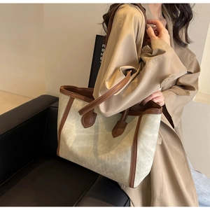 Maillard style beige tote bag with brown leather handles worn by a model in a studio