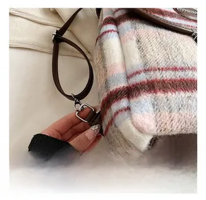 Detail showing the silver metal swivel hook and brown faux leather trim on plaid backpack