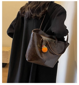 Close-up of a vintage dark brown tote bag featuring an orange knit orange charm accessory