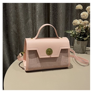 Pink two-tone handbag with gold rotary lock and adjustable strap on a beige table
