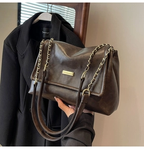 Detail of dark brown leather tote with golden rectangular buckle and chain strap