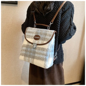 Detail of plaid wool backpack featuring brown leather trim and metal clasp closure