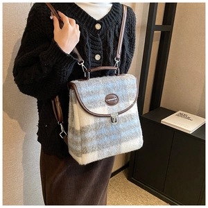 Close-up of blue plaid wool backpack with brown leather trim and metal twist lock