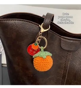 Detail of handmade crochet persimmon charm with golden metal clasp on a leather tote bag