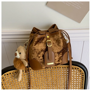 Détail du sac seau matelassé en velours marron avec base en cuir et breloque ours mignon