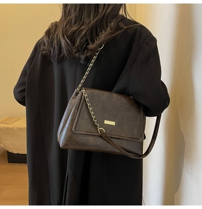 Detail shot of a dark brown vintage tote bag with gold buckle and chain strap on model