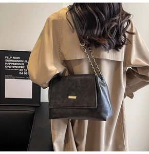 Detail of black vintage leather bag with gold buckle and chain strap on khaki coat