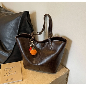 Detail of vintage brown leather tote bag with bright orange knit charm on stone