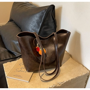 Detail view of deep brown leather tote bag with orange persimmon knitted charm