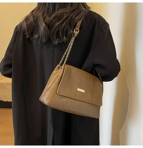 Close-up of brown leather tote bag with metallic bar and chain strap on a model