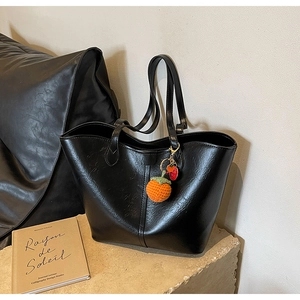 Detail of black tote bag with retro oil wax texture and handmade orange knit pendant charm
