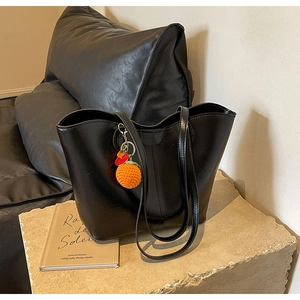 Detail of black faux leather tote bag with unique knitted orange pendant on stone base