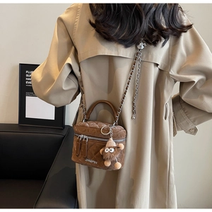 Detailed back view of a brown quilted crossbody bag with a plush monster charm on a trench coat